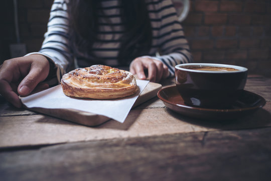 Closeup image of a woman holding a raisin danish with coffee cup on wooden vintage table in vintage coffee shop
