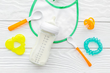 bottle with breastmilk and infant formula powdered healthy food, toys and bib on wooden background top view