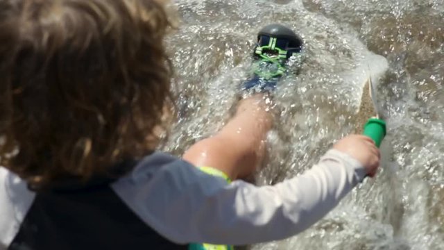 Little Boy Sits In Gentle Waves At Beach, Plays With Shovel, Slow Motion Closeup