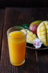Fresh tropical mango juice on table with mango fruits on background.