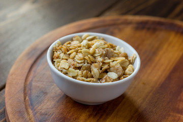 Granola or muesli in white ceramic bowl over wooden table.