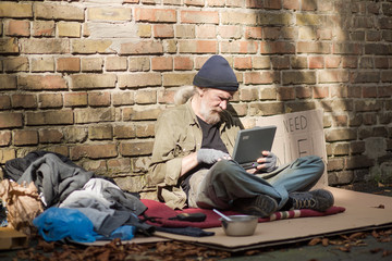 Modern world, even homeless people using modern technologies. Tramp living in the streets, using laptop.