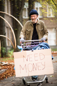 Homeless man with severe face in the street of the city. Tramp pushing shopping cart with his possessions.