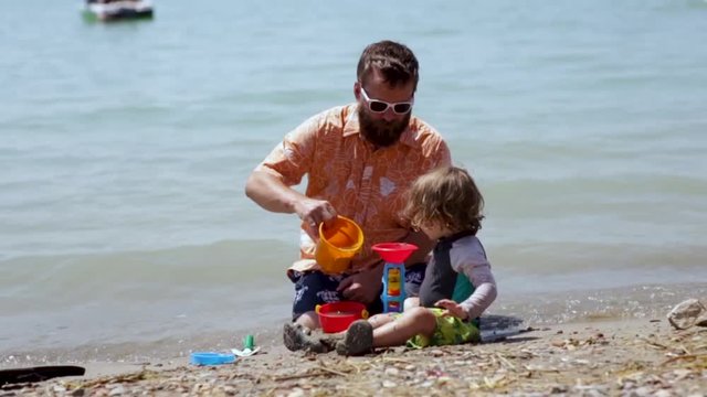 Father And Son Play With Sand Toys At Beach, Father Rinses Off His Sons Sandy Legs 