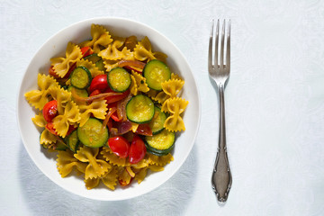 Whole farfalle pasta with zucchini, cherry tomatoes and red onion seen from above