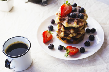 Plate of waffles and berries with cup of coffee
