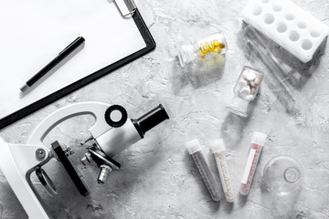 Laboratory test. Microscope, pills, test tube on grey stone background top view