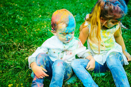 little girl with boy sit on the ground all dirty in holi paints