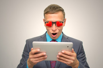 Online Dating. Fall in love. Womanizer man. Man in suit, heart shape glasses and wide open mouth looking on tablet computer screen and admires of beautiful lady.