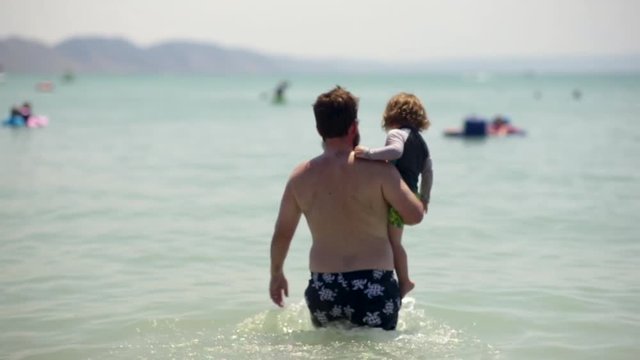 Father Carries His Little Boy Into Water, To Go For A Swim Together, Slow Motion