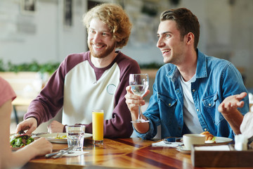 Cheerful group of friends gathered together at modern restaurant, enjoying delicious food and chatting animatedly with each other