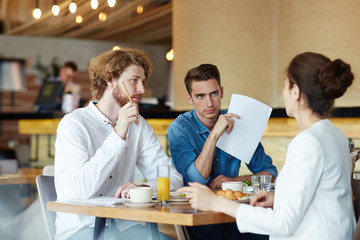 Unrecognizable young designer sharing ideas concerning start-up project with her handsome colleagues while having working meeting at modern cafe, blurred background