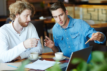 Fototapeta premium Group of young entrepreneurs gathered together at cozy coffeehouse and preparing for important negotiations with business partners, blurred background