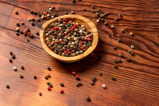 Peppercorns in a wooden bowl on a dark wooden background