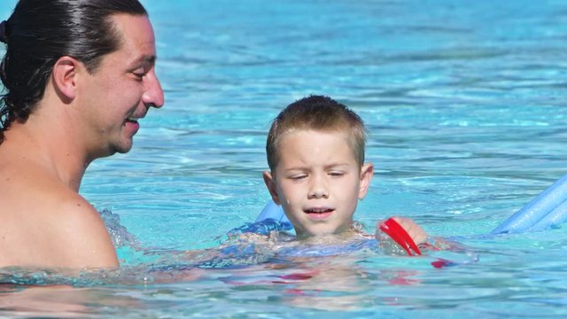 Young son playing in the pool with his father