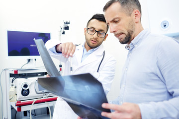 Two men, ragiologist and patient, looking at x-ray images during appointment