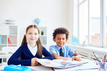 Two little classmates with open book reading in group