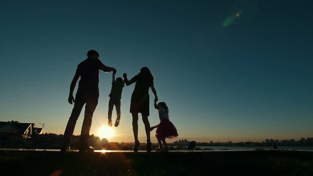 Happy family - father, mother, daughter and little son - silhouette at sunset, slow-motion