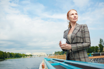 Serene businesswoman with drink enjoying solitude on steamer by riverside