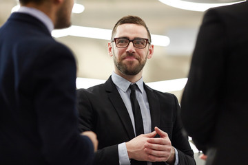 Confident financier in formalwear listening to one of colleagues at meeting