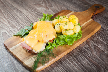 Beef steak with bacon and cheese on a wooden board with greens and potatoes