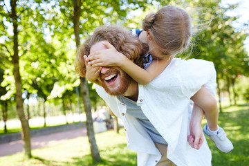 Fototapeta premium Laughing man holding his daughter on back during play in park