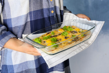 Woman holding baking dish with broccoli casserole on light background