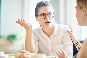 Anxious woman explaining reason of her worry to friend by cup of coffee