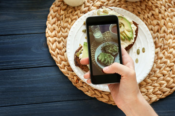 Young woman taking photo of delicious toasts with mobile phone