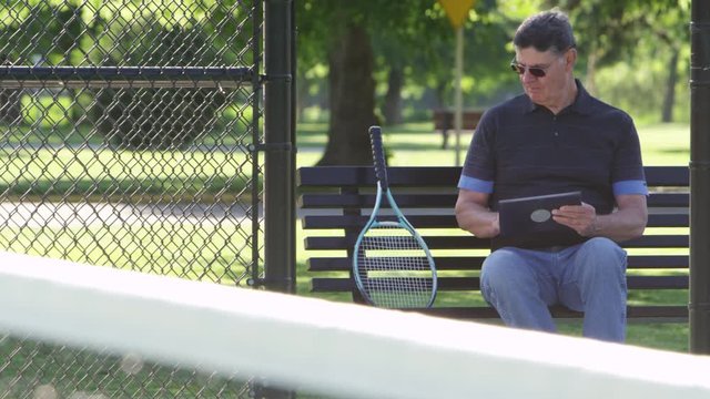 Portrait of elderly man at the tennis court with tablet