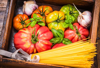 Tomatoes and spaghetti pasta on rustic wood background.