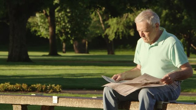 Portrait of elderly man reading newspaper in the park