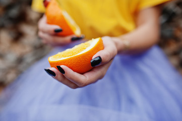 Two pieces of orange at in girl hands with black manicure.