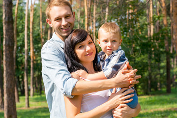 Dad hugs mom who holds the child in her arms. Happy family - Mom, Dad and child- for a walk in the park. Family resting in the park