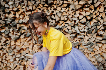 Obraz na płótnie Canvas Young funny girl with bright make-up, like fairytale princess, wear on yellow shirt and violet skirt against wooden background.