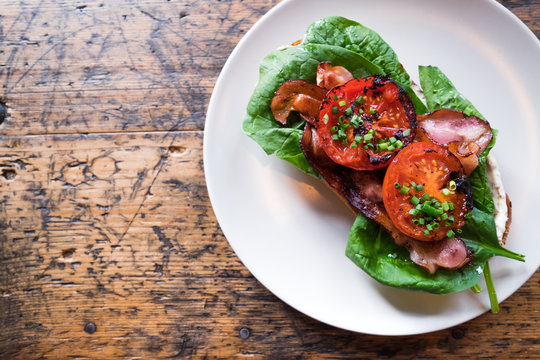 Plate with BLT toast with grilled tomatoes, bacon, lettuce and special sauce on the old wooden table top view