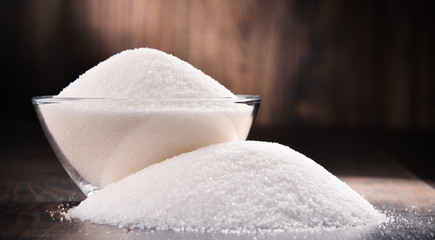 Composition with bowl of white refined sugar on wooden table