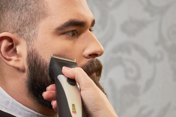 Beard grooming, hand with trimmer. Client of barber shop.