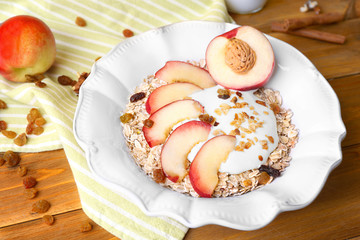 Tasty dessert with muesli, yogurt and peaches in plate on wooden table