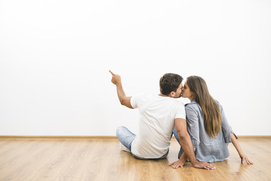 The sitting couple kissing on the empty wall background