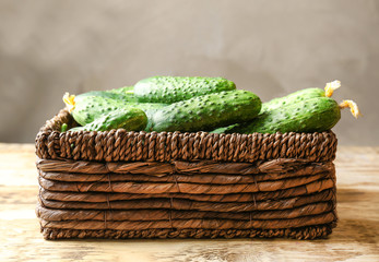 Many green fresh cucumbers in wicker basket on wooden table