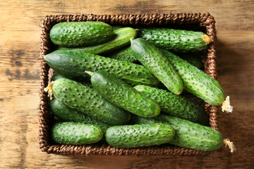 Many green fresh cucumbers in wicker basket on wooden table
