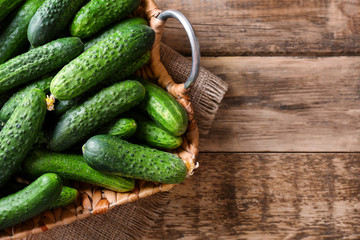 Many green fresh cucumbers in wicker basket on wooden table