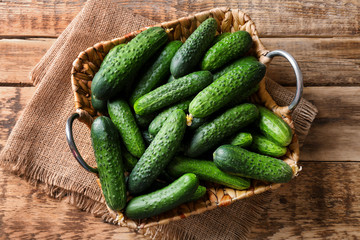 Many green fresh cucumbers in wicker basket on wooden table