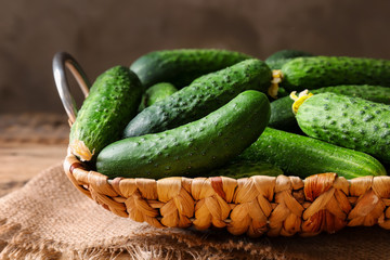 Many green fresh cucumbers in wicker basket on table
