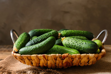 Many green fresh cucumbers in wicker basket on table