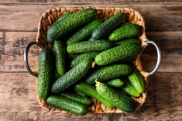 Many green fresh cucumbers in wicker basket on wooden table