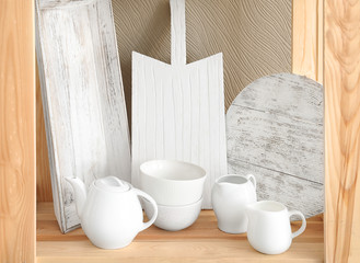 Wooden storage stand with ceramic dishware on color background