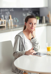 Young woman with orange juice and tablet in kitchen.