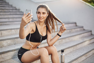 Female running traner taking a selfie with a smart phone listening to rock music in her white wired...